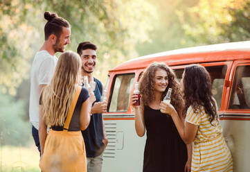 Eine Gruppe junger Freunde mit Getränken steht auf einem Roadtrip durch die Landschaft im Freien und hält Flaschen in der Hand. - HPIF24751