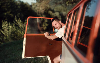 Ein fröhlicher junger Mann, der auf einem Roadtrip durch die Landschaft aus einem Auto aussteigt. Platz kopieren. - HPIF24757