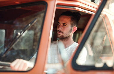 Ein fröhlicher junger Mann am Steuer eines Autos auf einer Fahrt durch die Landschaft. - HPIF24758