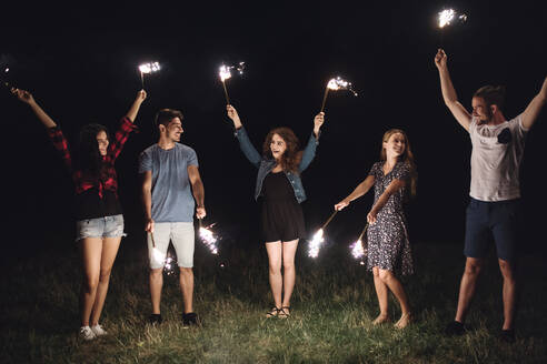 Eine Gruppe junger Freunde mit Wunderkerzen steht in der Abenddämmerung auf einem Roadtrip durch die Landschaft. - HPIF24771