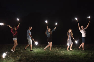 Eine Gruppe junger Freunde mit Wunderkerzen steht in der Abenddämmerung auf einem Roadtrip durch die Landschaft. - HPIF24772