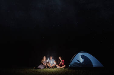 Friends with sparklers outdoors at dusk and one with smartphone in tent, concept of technology addiction versus adventure experience. Copy space. - HPIF24774