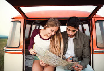 A young couple on a roadtrip through countryside, sitting in retro minivan and looking at a map. - HPIF24786