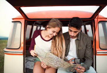 Ein junges Paar auf einem Roadtrip durch die Landschaft, das in einem Retro-Minivan sitzt und auf eine Landkarte schaut. - HPIF24786