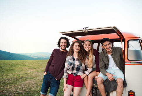A group of young friends on a roadtrip through countryside, standing by a retro minivan. - HPIF24791