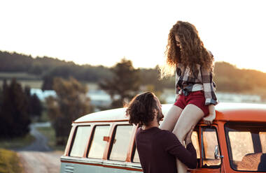 A young couple on a roadtrip through countryside, standing by retro minivan. - HPIF24793