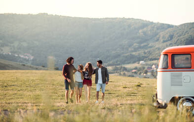 Eine Gruppe junger Freunde in einem Retro-Minivan auf einem Roadtrip durch die Landschaft, die Arm in Arm gehen. - HPIF24796