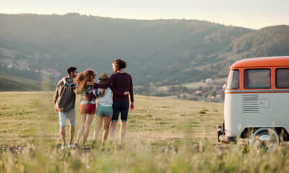 A rear view of group of young friends on a roadtrip through countryside, walking arm in arm. - HPIF24797