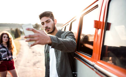 Ein junges Paar auf einem Roadtrip durch die Landschaft, das sein Abenteuer mit einem Selfie auf dem Smartphone festhält - HPIF24803