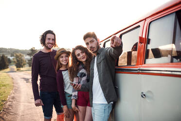 Eine Gruppe junger Freunde auf einem Roadtrip durch die Landschaft, die neben einem Retro-Minivan stehen. - HPIF24805