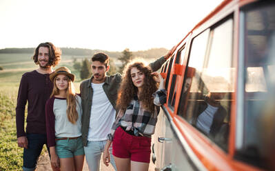 Ein Porträt einer Gruppe junger Freunde, die auf einem Roadtrip durch die Landschaft neben einem Retro-Minivan stehen. - HPIF24808