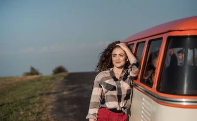 Ein junges Mädchen auf einem Roadtrip durch die Landschaft, das sich auf einen Retro-Minivan stützt. Platz kopieren. - HPIF24816