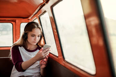 Friends on a roadtrip through countryside, a girl with headphones and smartphone listening to music. Copy space. - HPIF24832