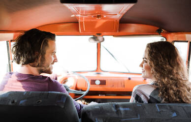 A rear view of young couple on a roadtrip through countryside, driving retro minivan. - HPIF24840