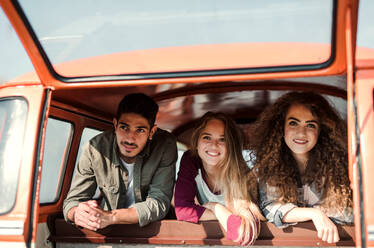 Eine Gruppe fröhlicher junger Freunde mit einem Retro-Minivan auf einem Roadtrip durch die Landschaft, die aus dem Fenster schauen. - HPIF24847