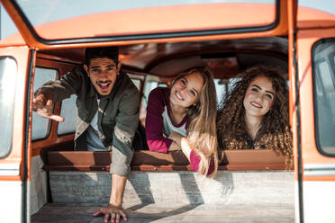 Eine Gruppe fröhlicher junger Freunde mit einem Retro-Minivan auf einem Roadtrip durch die Landschaft, die aus dem Fenster schauen. - HPIF24848