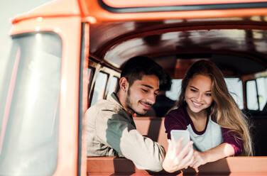A group of young friends standing by a retro minivan on a roadtrip through countryside, taking selfie with smartphone. - HPIF24851