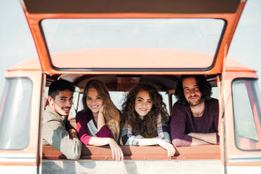 Eine Gruppe fröhlicher junger Freunde mit einem Retro-Minivan auf einem Roadtrip durch die Landschaft, die aus dem Fenster schauen. - HPIF24853
