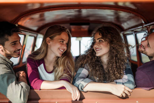 Eine Gruppe fröhlicher junger Freunde mit einem Retro-Minivan auf einem Roadtrip durch die Landschaft, in einem Auto sitzend. - HPIF24856