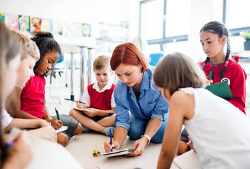 Eine Gruppe kleiner Schulkinder mit Lehrer, die in der Klasse auf dem Boden sitzen und Naturwissenschaften lernen. - HPIF24862