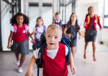 Ein Schuljunge mit Down-Syndrom, der eine Tasche trägt, und eine Gruppe von Kindern, die durch den Flur rennen. - HPIF24863