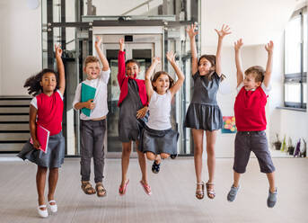 A group of cheerful small school kids in corridor, jumping. Back to school concept. - HPIF24869