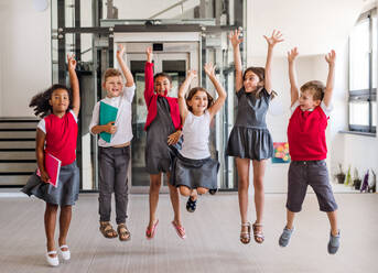 Eine Gruppe fröhlicher kleiner Schulkinder im Korridor, die springen. - HPIF24869