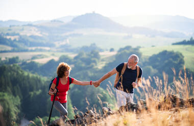 Ein älteres Touristenpaar mit Rucksäcken wandert bei Sonnenuntergang in der Natur und hält sich an den Händen. - HPIF24895