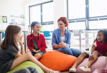 A group of small school kids with teacher sitting on bean bags in class, talking. - HPIF24919