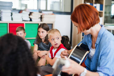 Ein Junge mit Down-Syndrom sitzt mit Schülern und Lehrern in der Klasse auf dem Boden und spielt Gitarre. - HPIF24921