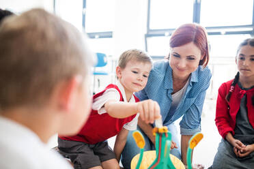 Eine Gruppe kleiner Schulkinder mit Lehrer, die in der Klasse auf dem Boden sitzen und Naturwissenschaften lernen. - HPIF24927