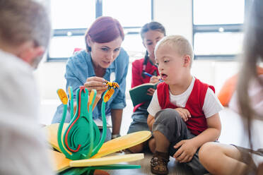 Eine Gruppe kleiner Schulkinder mit Lehrer, die in der Klasse auf dem Boden sitzen und Naturwissenschaften lernen. - HPIF24929