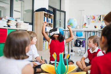 Eine Gruppe kleiner Schulkinder mit VR-Brillen sitzt im Unterricht auf dem Boden und lernt Wissenschaft. - HPIF24930