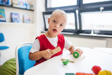 Ein glücklicher Schuljunge mit Down-Syndrom, der am Schreibtisch im Klassenzimmer sitzt und lernt. - HPIF24931