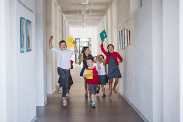 Eine Gruppe fröhlicher kleiner Schulkinder im Korridor, die rennen und springen - ein Konzept für den Schulanfang. - HPIF24947