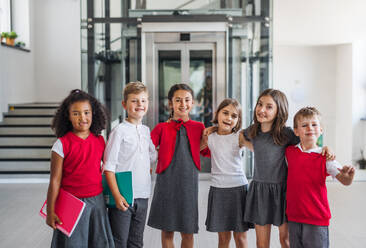 Eine Gruppe fröhlicher kleiner Schulkinder auf dem Flur, die in die Kamera schauen - ein Konzept für den Schulanfang. - HPIF24953