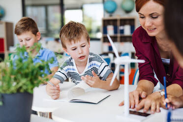 Eine Gruppe von kleinen Schulkindern mit einem Lehrer, die in einem Kreis am Schreibtisch sitzen und Wissenschaft lernen. - HPIF24955