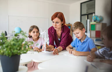 Eine Gruppe von kleinen Schulkindern mit einem Lehrer, die in einem Kreis am Schreibtisch sitzen und Wissenschaft lernen. - HPIF24957