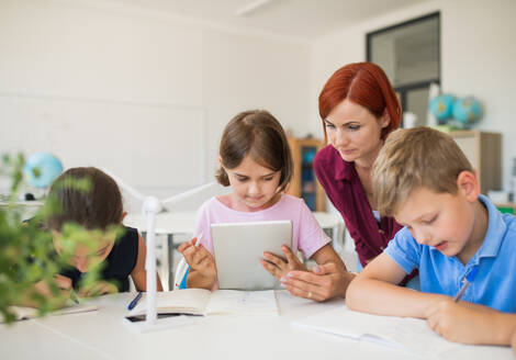 Eine Gruppe kleiner Schulkinder mit Lehrer, die im Kreis sitzen und ein Tablet benutzen. - HPIF24959