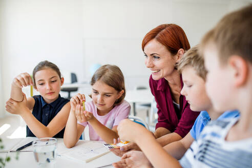 Eine Gruppe kleiner Schulkinder mit Lehrer, die in der Klasse auf dem Boden sitzen und Naturwissenschaften lernen. - HPIF24961