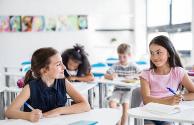 Small school children sitting at the desk in classroom on the lesson, talking. - HPIF24977