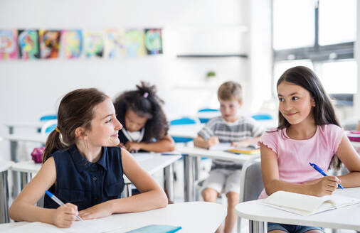 Kleine Schulkinder, die im Klassenzimmer am Schreibtisch sitzen und sich unterhalten. - HPIF24977
