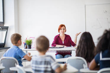 Rear view of school children sitting at the desk in classroom on the lesson, listening to teacher. - HPIF24985