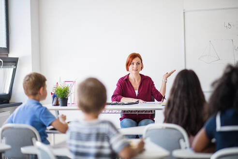 Rückansicht von Schulkindern, die im Klassenzimmer auf dem Schreibtisch sitzen und dem Lehrer zuhören. - HPIF24985