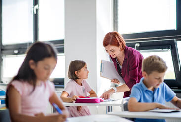 A friendly teacher walking among small school children on the lesson, explaining and helping. - HPIF24988