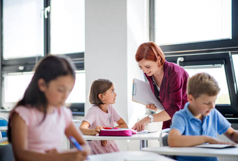 Ein freundlicher Lehrer, der im Unterricht zwischen kleinen Schulkindern umhergeht, erklärt und hilft. - HPIF24988