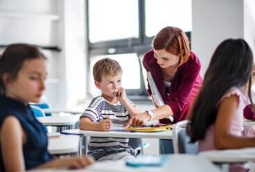 Ein freundlicher Lehrer, der im Unterricht zwischen kleinen Schulkindern umhergeht, erklärt und hilft. - HPIF24989