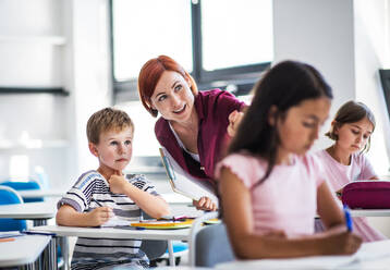 Ein freundlicher Lehrer, der im Unterricht zwischen kleinen Schulkindern umhergeht, erklärt und hilft. - HPIF24990