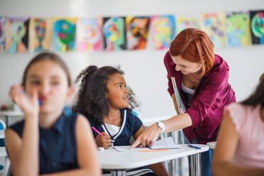 A friendly teacher walking among small school children on the lesson, explaining and helping. - HPIF24992