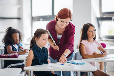 Ein freundlicher Lehrer, der im Unterricht zwischen kleinen Schulkindern umhergeht, erklärt und hilft. - HPIF24993